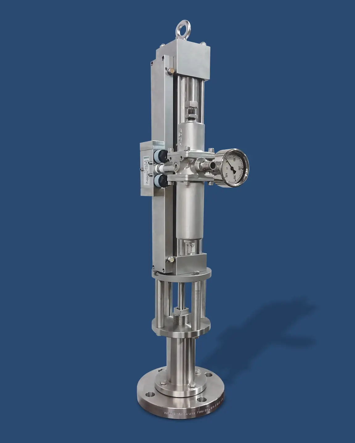 A vertical industrial machine with a robust metallic structure, featuring cylindrical components and a top-head drive pump, a gauge on the right side, and multiple small pipes and fittings. The base is a round metallic platform, set against a solid blue background.