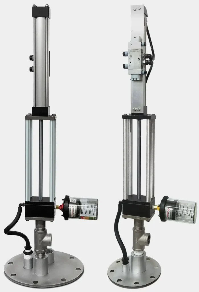 Two industrial pneumatic cylinders with connected components, including gauges and black tubing, are displayed side by side on circular metal bases. Featuring vertical metal rods and grey cylindrical bodies, the setup integrates a top-head drive pump among various mechanical parts attached.